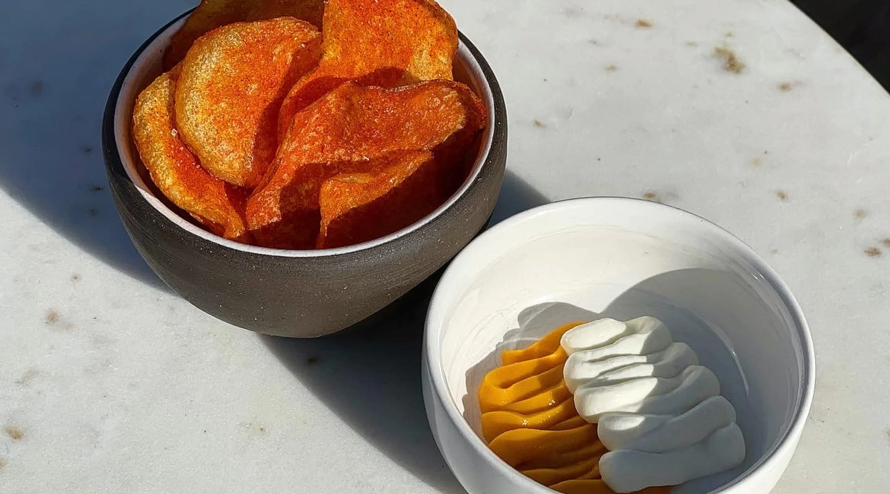 Brown bowl with chips and  white bowl with sauces.