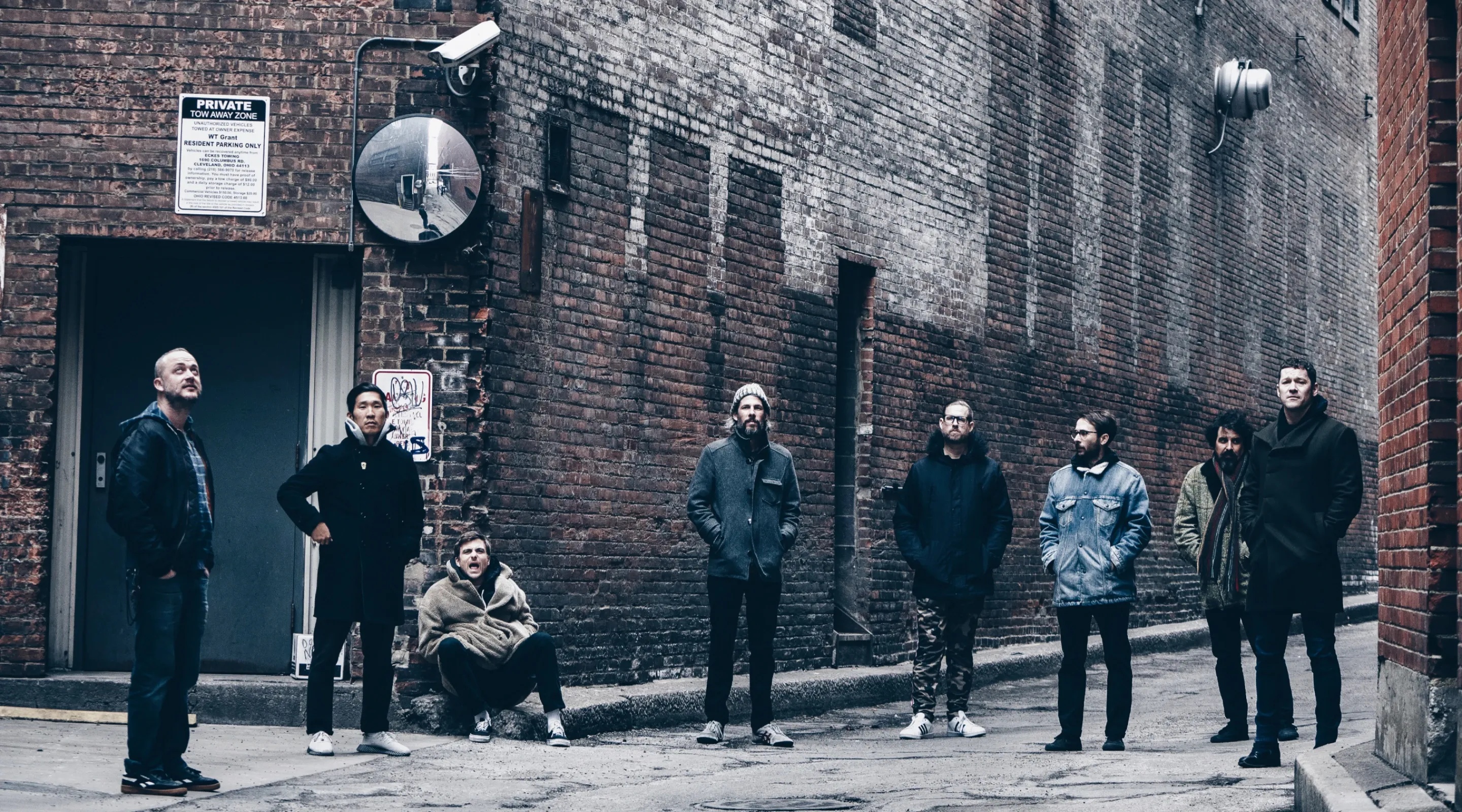 Image of eight men in an alley wearing coats.