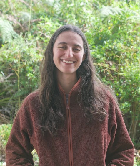Professional portrait with gray background A woman with long hair smiling while wearing a rust-colored jacket.