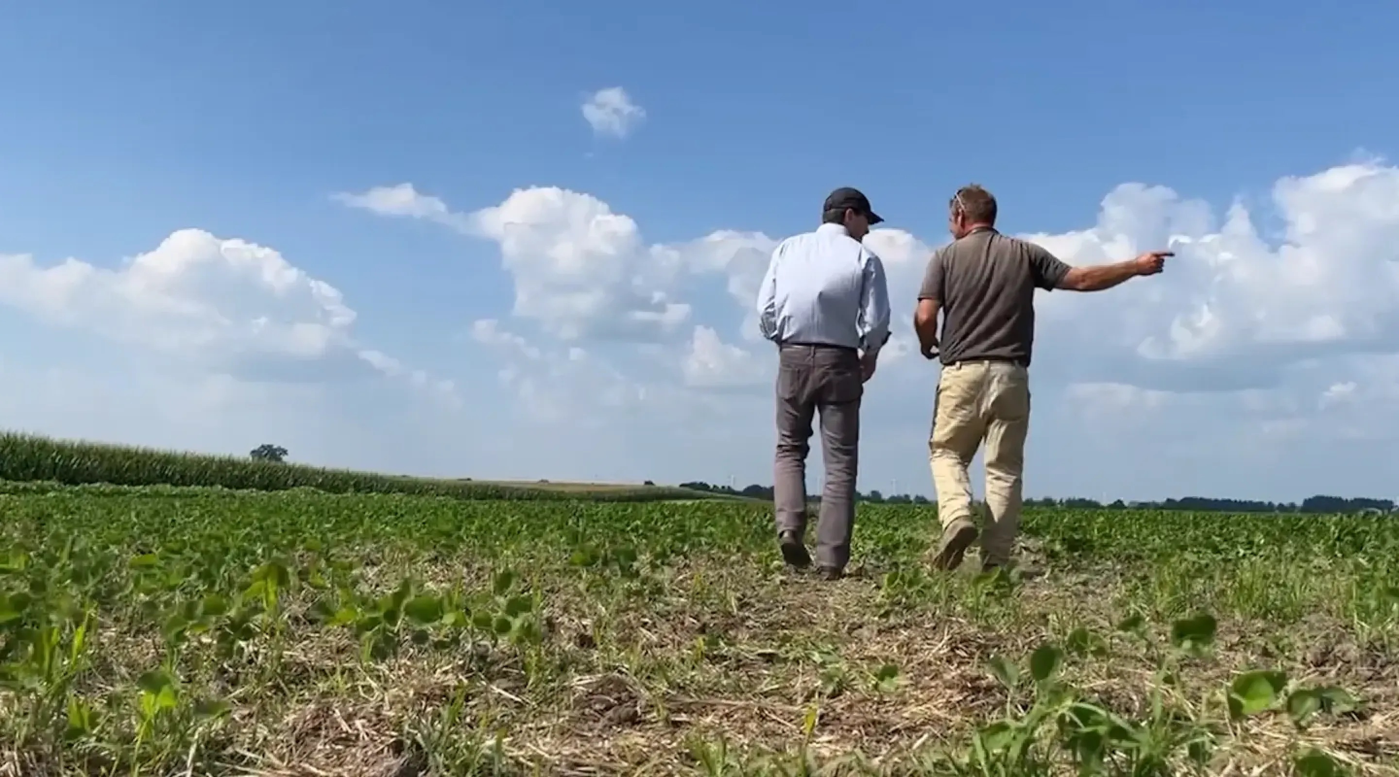 orion-carousel-bg.webp Two men walking through a crop field under a clear blue sky, facing away from the camera as they engage in conversation.